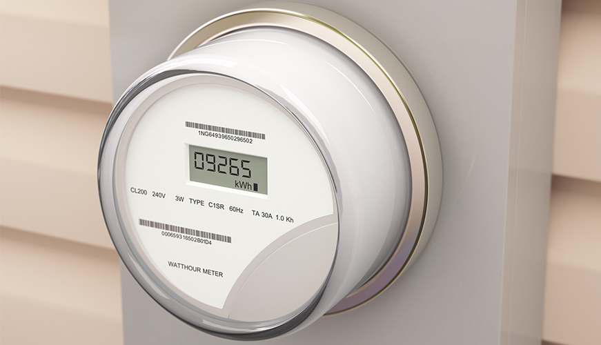 A digital electricity meter mounted on a wall shows a reading of 09265 kWh. The meter is protected by a transparent cover, with visible labels indicating its specifications and type.